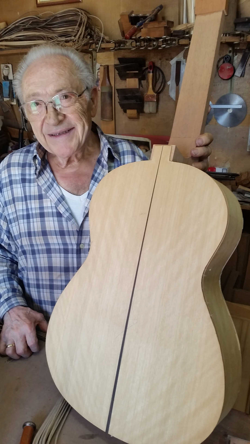 Man holding a wooden guitar in a workshop setting