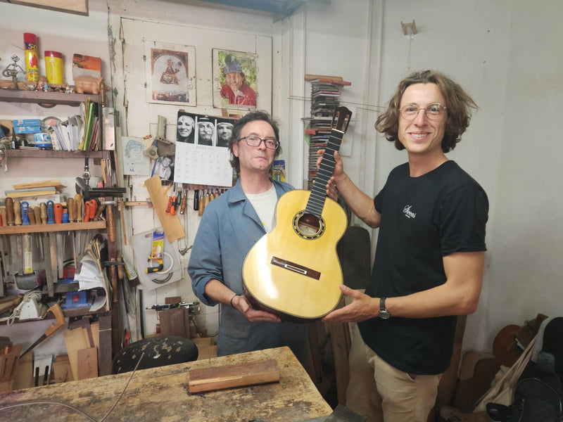 Two men in a workshop holding a yellow guitar