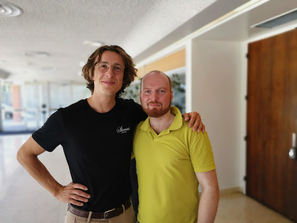 Two men standing together in an indoor setting with a neutral background