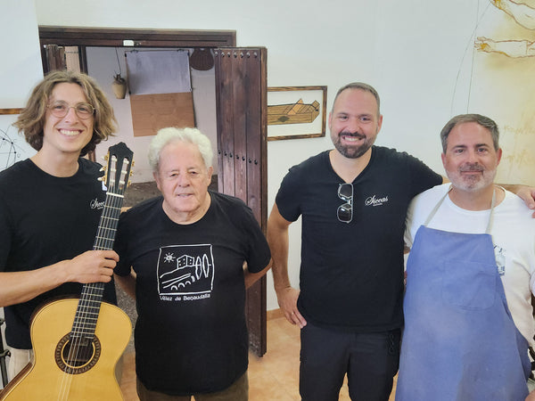 Four men posing together in a room with one holding a guitar