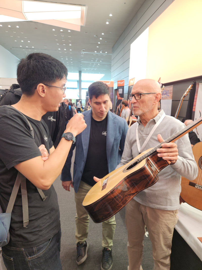 Three men interacting with a guitar in an indoor setting, possibly a store or exhibition.