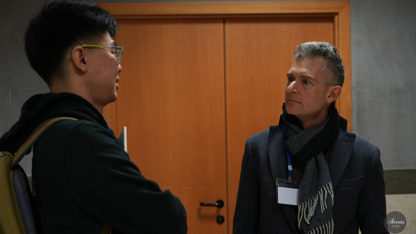 Two men are having a conversation in a room with a wooden door.