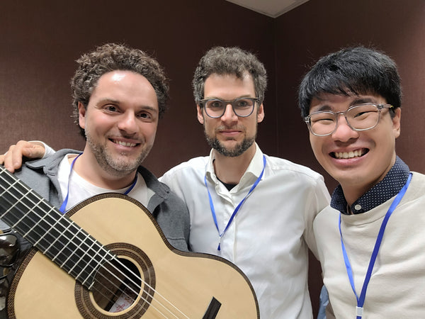 Three men posing together with a guitar in an indoor setting