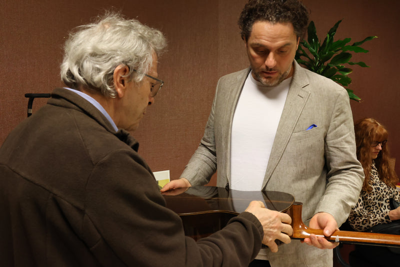 Two men examining a wooden object in an indoor setting