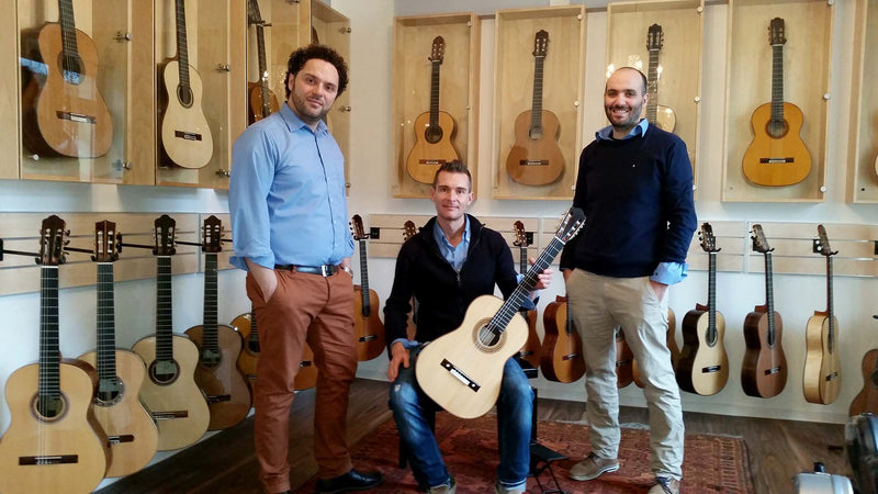 Three men posing with a guitar in a room filled with guitars at Siccas Guitars