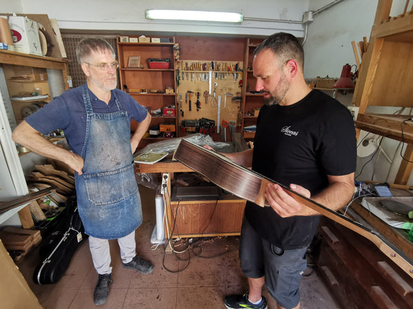Two men in a workshop, one holding a long wooden object.