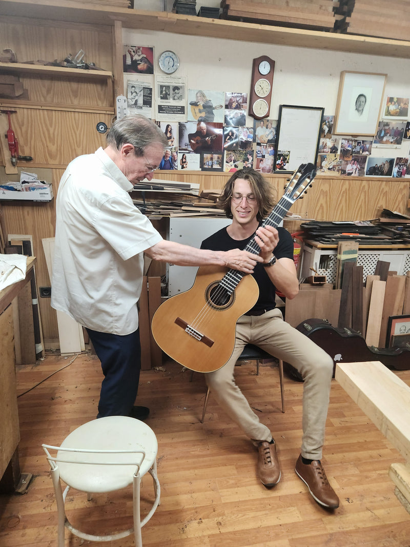 Two men in a workshop with one holding a guitar